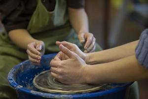 The potter teaches the craft to the child. Close-up of a potter's hands and a child's hand with a product on a potter's wheel. Working with clay. Clay master class. photo