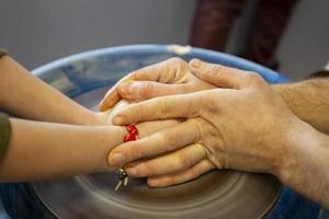 Close-up of a potter's hands and a child's hand with an item on a potter's wheel. Working with clay. Clay workshop. Craft training. photo