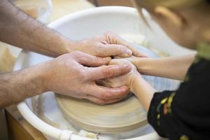 The potter teaches the craft to the child. Close-up of a potter's hands and a child's hand with a product on a potter's wheel. Working with clay. Clay master class. photo