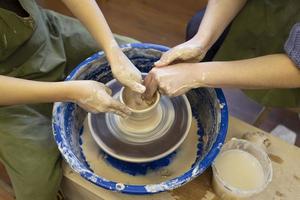 Close-up of a potter's hands and a child's hand with an item on a potter's wheel. Working with clay. Clay workshop. Craft training. photo