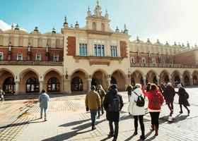 Krakow, Poland, 2023 - guide with tour group in main square in Krakow. Free tourist walking tours with locals. Unique experience in new city. The cloth hall for souvenir photo