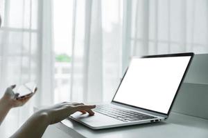 Woman hands using laptop with blank screen on white table at home or office. photo