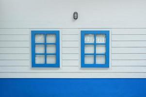 Two windows on white wood wall, outdoor view. Colorful blue window from front outside of house. photo