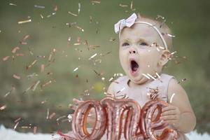 A funny little girl in a bright confetti yawns. Bored child at the birthday party. Beautiful baby. photo