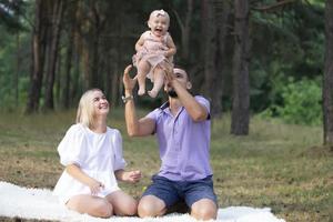 marido, esposa y su pequeño hija para un caminar en el parque. contento papá y mamá sacudida arriba su pequeño hija. foto