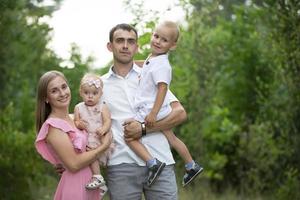 Husband and wife and their little children. Family portrait in nature. Mom and Dad are posing with their brother and sister. Young family with children for a walk in the woods. photo