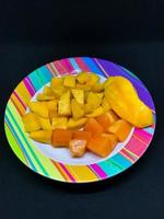 slices of mango and papaya fruit on a colorful motif plate photo