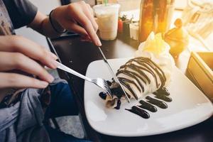 el dulce postre chocolate plátano crepes con oro hilos Adición y un taza de caliente latté café. foto