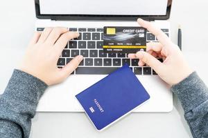 manos femeninas escribiendo en una computadora portátil con pasaporte y tarjeta de crédito foto