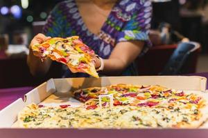 Woman hand taking a slice of New York pizza in takeaway box. photo