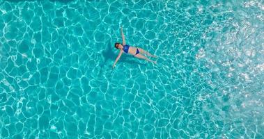 Top down view of a woman in a blue swimsuit lying on her back in the pool.
