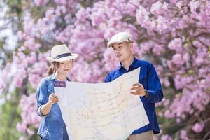 asiático Pareja turista participación ciudad mapa mientras caminando en el parque a Cereza florecer árbol durante primavera sakura flor festival concepto foto