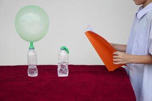 Closeup student study science experiment about reaction of chemical in bottles and balloons. Read  the result of experiment in book. Concept, science subject activity, education. Learning by doing photo