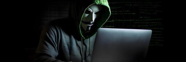 Unveiling the Enigmatic World of Cybercrime. A White Masked Hacker's Front View Amidst Dark Hood and Green Matrix Code Background photo