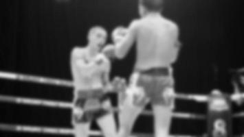 Blurred images black and white photo style of Thai boxing or Muay Thai or Kickboxing which local and foriegn boxer are fighting on the ring at indoor stage as martial art sport. Muay Thai Kick boxing