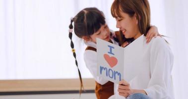 un pequeño hija dando mamá hecho a mano saludo tarjeta y deseando su contento de la madre día. foto