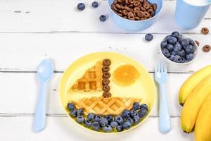 Boat of waffles with blueberries on a white wooden background. Funny food idea for kids. photo