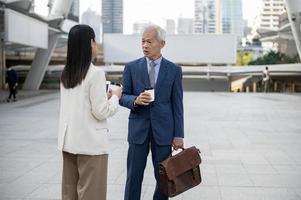 Asian senior mature middle aged businessman and young businesswoman having a discussion and coffee in modern city photo