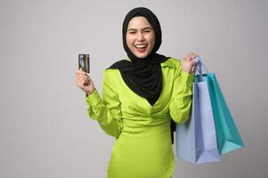 Beautiful musllim woman with hijab holding credit card and shopping bag over white background studio, shopping and finance concept. photo