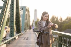 Portrait of young business woman with an electric scooter to work over bridge in modern city  background photo