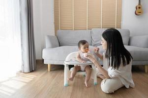 joven madre Ayudar bebé comiendo mezcla comida en bebé silla foto