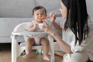 joven madre Ayudar bebé comiendo mezcla comida en bebé silla foto