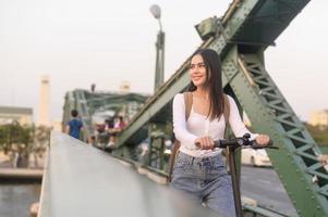 Portrait of young beautiful woman with an electric scooter  over bridge in modern city  background photo