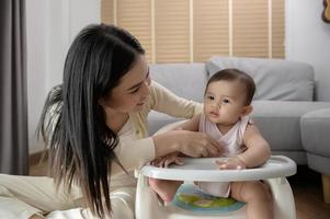 joven madre Ayudar bebé comiendo mezcla comida en bebé silla foto