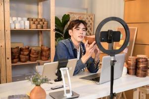 A young Asian man entrepreneur live streaming to sale craft products  to customers in his shop , Technology online business concept. photo