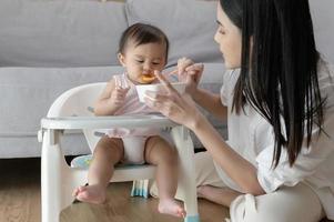 joven madre Ayudar bebé comiendo mezcla comida en bebé silla foto