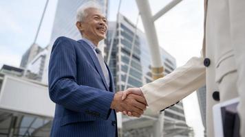 Asian senior mature middle aged businessman handshaking young businesswoman in modern city photo