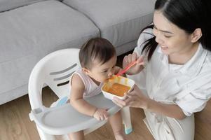 Young mother helping baby eating blend food on baby chair photo