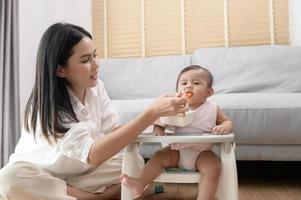 joven madre Ayudar bebé comiendo mezcla comida en bebé silla foto