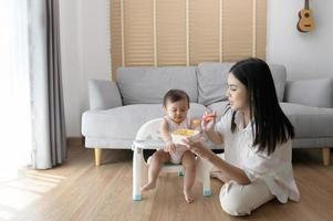 joven madre Ayudar bebé comiendo mezcla comida en bebé silla foto