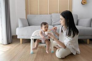 joven madre Ayudar bebé comiendo mezcla comida en bebé silla foto