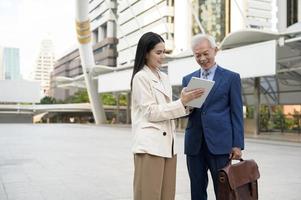 Asian senior mature middle aged businessman and young businesswoman having a discussion and using tablet in modern city photo