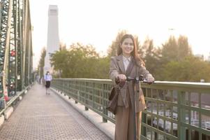 Portrait of young business woman with an electric scooter to work over bridge in modern city  background photo