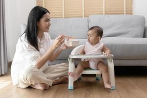 joven madre Ayudar bebé comiendo mezcla comida en bebé silla foto