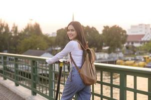 retrato de joven hermosa mujer con un eléctrico scooter terminado puente en moderno ciudad antecedentes foto