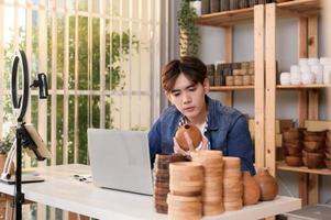 A young Asian man entrepreneur live streaming to sale craft products  to customers in his shop , Technology online business concept. photo