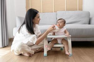 Young mother helping baby eating blend food on baby chair photo