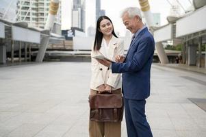 asiático mayor maduro medio Envejecido empresario y joven mujer de negocios teniendo un discusión y utilizando tableta en moderno ciudad foto