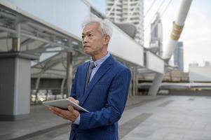 Asian senior mature middle aged businessman using tablet in modern city photo