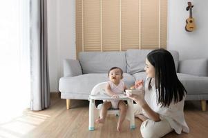 joven madre Ayudar bebé comiendo mezcla comida en bebé silla foto