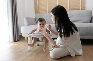 joven madre Ayudar bebé comiendo mezcla comida en bebé silla foto