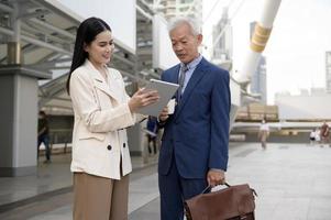Asian senior mature middle aged businessman and young businesswoman having a discussion and using tablet in modern city photo