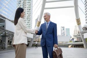 Asian senior mature middle aged businessman handshaking young businesswoman in modern city photo