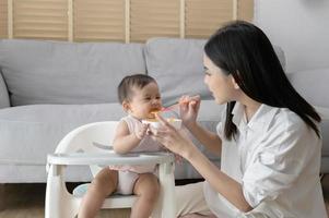 Young mother helping baby eating blend food on baby chair photo