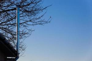 Thin chrome chimney on the roof against the blue sky and wood in winter. Horizontal. Photo in high quality