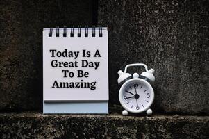 Motivational and inspirational quote on notepad - Today is a great day to be amazing. With rock and alarm clock background. photo